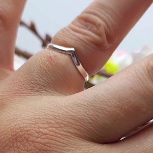 May include: A silver ring with a V-shaped design. The ring is worn on a finger.