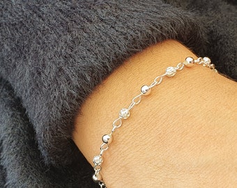 Puede incluir: Una pulsera de cadena plateada con un patrón repetitivo de cuentas redondas lisas y pulidas que se alternan con cuentas esféricas más pequeñas, texturizadas y facetadas, unidas por delicados eslabones de plata para una pieza refinada.