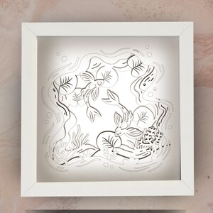 May include: White frame with a white background and a black paper cut-out design of two fish swimming in a pond with lily pads and water plants.