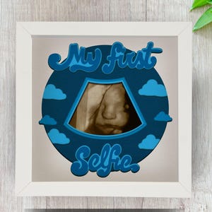 May include: A white frame with a blue and white design featuring a sonogram image and the text "My First Selfie".