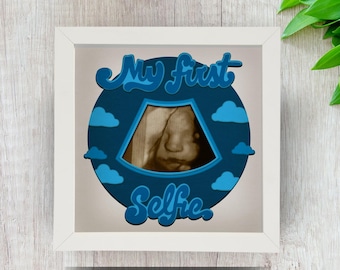 May include: A white frame with a blue and white design featuring a sonogram image and the text "My First Selfie".