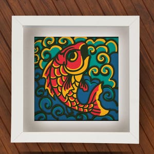 Peut inclure: Un cadre carré blanc contenant une œuvre d'art en papier superposé représentant un poisson koï stylisé rouge, jaune et orange nageant au milieu de motifs d'eau tourbillonnants bleus et sarcelle. L'œuvre a un aspect dimensionnel découpé.