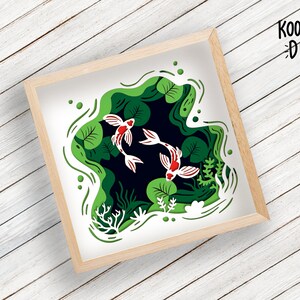 May include: A paper cut-out art design featuring three white and red fish swimming in a green pond with lily pads. The design is framed in a light wood frame.