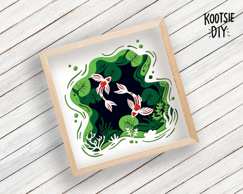 May include: A paper cut-out art design featuring three white and red fish swimming in a green pond with lily pads. The design is framed in a light wood frame.