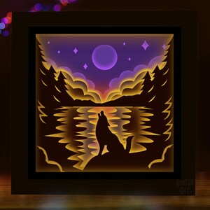 May include: A layered paper art piece depicting a wolf howling at the moon over a lake. The scene features a purple sky with stars, silhouetted trees, and a warm, glowing light effect. The artwork is framed in a black box.