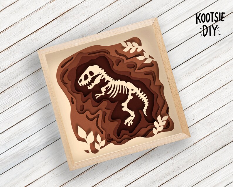 Pode incluir: Um esqueleto de dinossauro de papel castanho num quadro de papel em camadas. O quadro &eacute; feito de papel castanho e tem um fundo branco. O esqueleto de dinossauro est&aacute; em p&eacute; com a cabe&ccedil;a inclinada para o lado. O quadro tem o texto "KOOTSIE DIY" no canto superior direito.