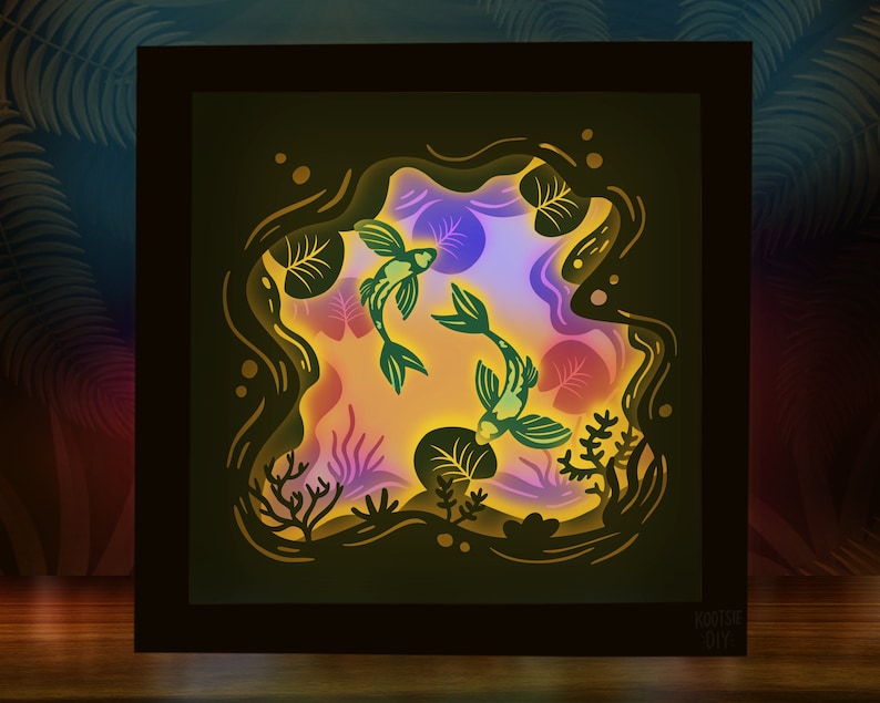 May include: A 3D paper cut-out art piece depicting two green fish swimming in a pond with lily pads and other aquatic plants. The art piece is illuminated from behind, creating a glowing effect.