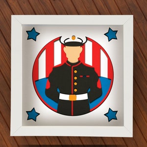 May include: A white frame with a red, white, and blue circle inside. The circle has a silhouette of a person in a military uniform with a hat. There are stars in the corners of the frame.
