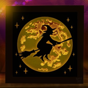 May include: A square shadow box frame featuring a layered paper cutout of a witch flying on a broomstick against a large, illuminated yellow moon. The scene includes small star cutouts in the black border and the text ROOTSIE DIY.