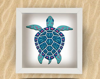 May include: A framed, decorative sea turtle art piece. The turtle features a teal head and flippers with pink and teal accents. The shell is a geometric design in shades of blue and white. The artwork is set against a white background and framed in a white square frame.