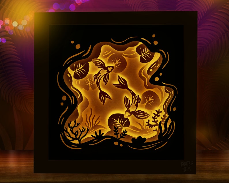 May include: A black framed 3D paper art piece depicting two gold fish swimming in a pond with lily pads. The fish are cut out and layered to create a 3D effect. The background is a dark blue with white stars.