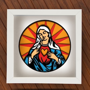Könnte beinhalten: Gerahmtes religiöses Kunstwerk mit einer stilisierten Darstellung einer Heiligen mit Herz. Das Kunstwerk ist vor einem gelb-roten Sonnenstrahlendesign platziert und in einem weißen quadratischen Rahmen eingefasst. Die Heilige trägt ein blaues Gewand.