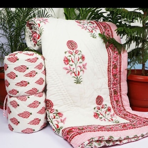 Puede incluir: Colcha de algod&oacute;n blanco con estampado floral rosa y una almohada a juego. La colcha tiene un borde de rayas rosa y blanco.