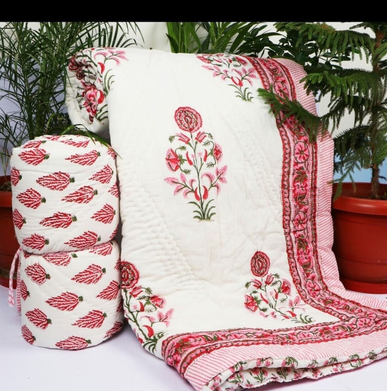 Puede incluir: Colcha de algod&oacute;n blanco con estampado floral rosa y una almohada a juego. La colcha tiene un borde de rayas rosa y blanco.