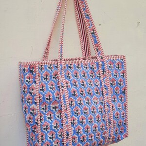 K&ouml;nnte beinhalten: Eine blaue und rosafarbene Blumentasche mit rot-wei&szlig; gestreiften Henkeln. Die Tasche hat einen Blumendruck und ist aus Baumwolle.