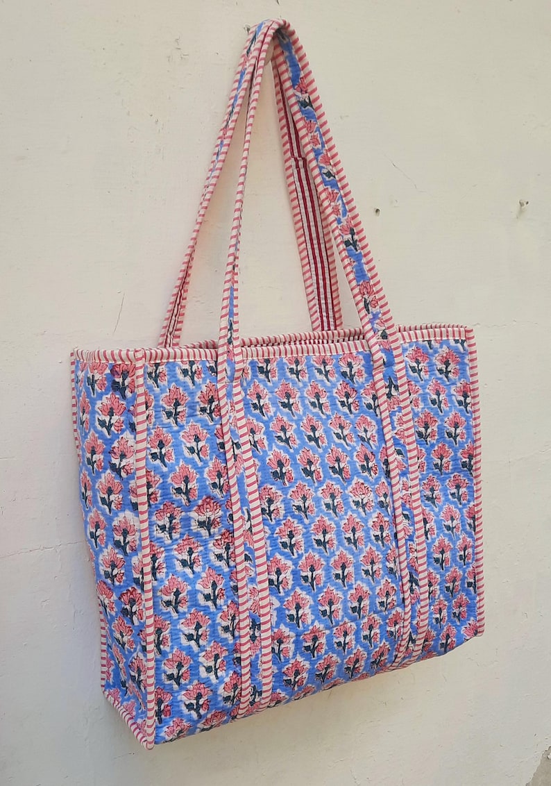 K&ouml;nnte beinhalten: Eine blaue und rosafarbene Blumentasche mit rot-wei&szlig; gestreiften Henkeln. Die Tasche hat einen Blumendruck und ist aus Baumwolle.