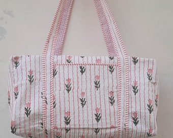 May include: A white and pink striped tote bag with a floral print. The bag has pink stitching and two handles.