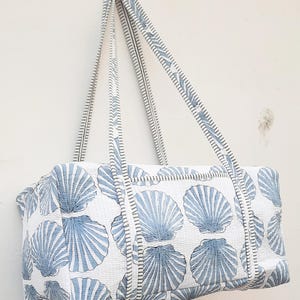 May include: A white tote bag with a blue seashell pattern. The bag has two long straps and a zip closure.
