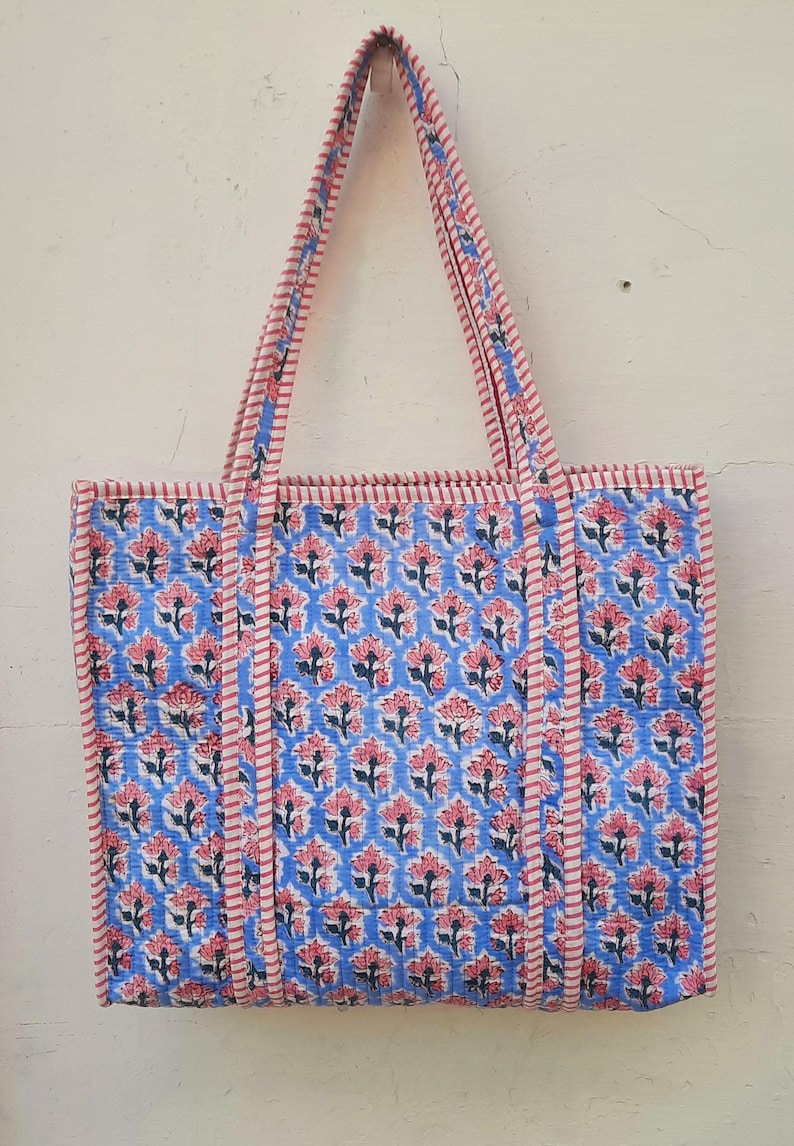K&ouml;nnte beinhalten: Eine blaue und rosafarbene Blumentasche mit wei&szlig;en Streifen an den Henkeln. Die Tasche ist aus Baumwolle und hat ein gestepptes Design.