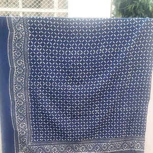May include: A navy blue textile with a white geometric pattern and floral border. The fabric is hanging, showcasing the detailed design. The pattern consists of small white shapes arranged in a repeating design.