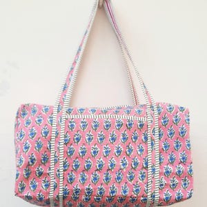 May include: A pink and blue floral print cotton tote bag with white and black striped straps.