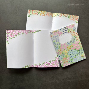 May include: Three small notebooks with floral designs on the covers. The notebooks are open to show the blank pages inside. The covers feature different floral patterns in pink, yellow, blue, and green.