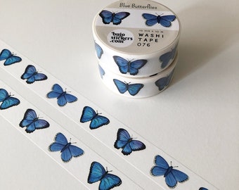 May include: Two rolls of blue butterfly washi tape. The tape is 15 mm wide and 10 m long. The tape is white with blue butterflies printed on it. The tape is labelled "Blue Butterflies" and "bujo stickers.com" and "WASH TAPE 076".