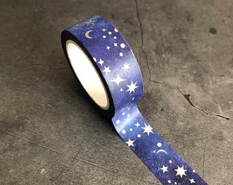 以下が含まれることがあります： 暗い青色の背景に、銀色の星、月、点で飾られた銀河柄の和紙テープのロールです。