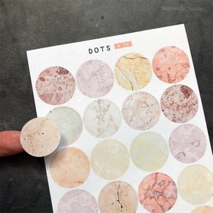 Puede incluir: Una hoja de 18 pegatinas redondas con estampado de mármol con el texto "DOTS 8 to 10" en la parte superior. Las pegatinas son de varios tonos de rosa, beige y marrón.