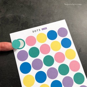 May include: A sheet of colourful round stickers with a white background. The stickers are in various colours, including yellow, pink, purple, blue, and green. The sheet is labelled "DOTS A 05".
