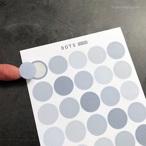 Puede incluir: Una hoja de pegatinas de puntos grises y blancos con el texto "DOTS A 09" impreso en la parte superior. Las pegatinas están dispuestas en una cuadrícula.
