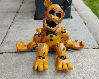 Op de afbeelding: Een geel animatronisch beren speelgoed met zwarte ogen en een zwarte hoge hoed. De beer zit met zijn benen gespreid en zijn armen uitgestrekt. Het speelgoed heeft een versleten en verweerde uitstraling.