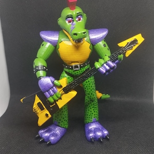 May include: A green alligator figurine with a yellow chest and purple accents, holding a yellow and black guitar. The figurine has a red mohawk and is wearing a black belt and wristbands. The alligator's skin is textured with green spots.