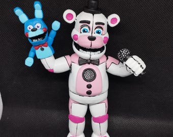 Puede incluir: Una figura animatrónica blanca y rosa con sombrero de copa negro y pajarita, sosteniendo un micrófono y una figura de conejo azul. La figura tiene detalles en rosa y una expresión amigable.