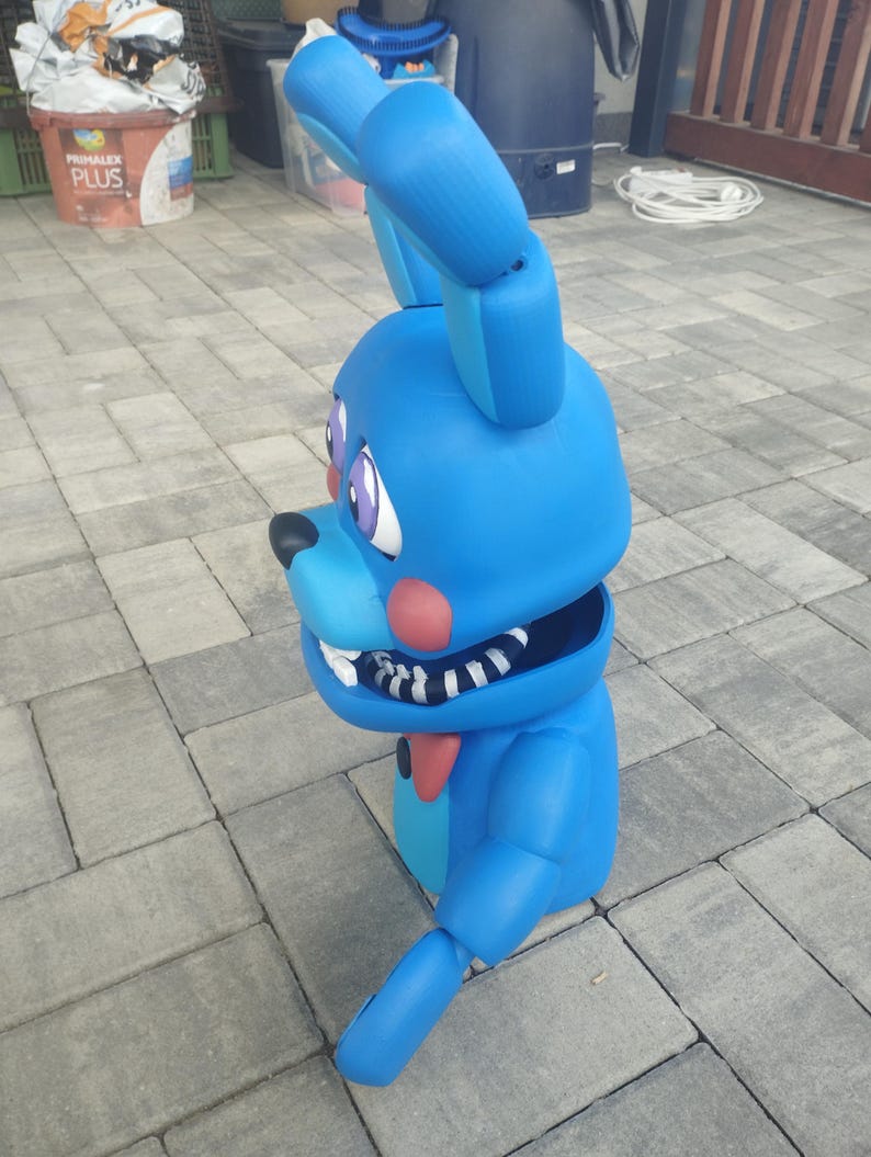 May include: A large, blue bunny figure with articulated limbs, large ears, and a red bow tie. The bunny has a black nose, pink cheeks, and purple eyes. The mouth is open, revealing white teeth. The figure is likely a character from a video game or cartoon.