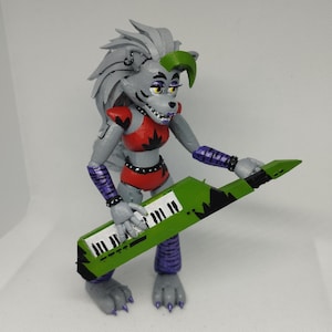 May include: A gray and green animatronic figure with a purple and black striped outfit, holding a green keyboard with black keys and black and white accents. The figure has a green mohawk and a red and black top.