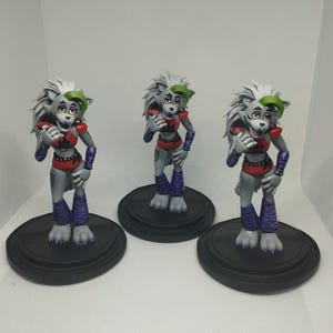 May include: Three gray and white wolf-like figures with green hair, red and black clothing, and purple and white striped legs. Each figure is standing on a black circular base.