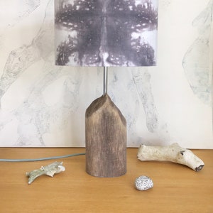 May include: A wooden table lamp with a grey and white patterned lampshade. The lamp is on a wooden table with a white background.