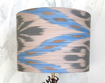 May include: A table lamp featuring a cylindrical lampshade with a blue, gray, and beige ikat pattern. The base is a large, textured, porous rock with a dark red organic accent near the brass stem. Several small, textured sea shells surround the base.