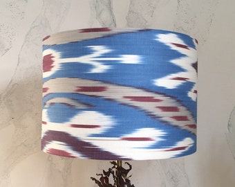 May include: A blue and white lampshade with a red and white ikat pattern. The lampshade is on a wooden base.