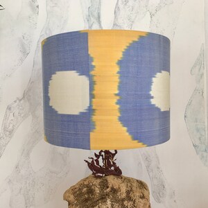May include: A blue and yellow lampshade with white circles, sitting on a natural stone base.
