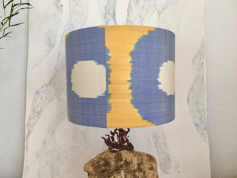 May include: A blue and yellow lampshade with white circles, sitting on a natural stone base.