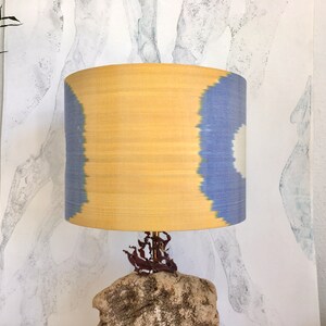 May include: A yellow and blue patterned lampshade with a natural stone base. The lampshade is made of fabric and has a unique ikat design. The base is made of a rough, textured stone.