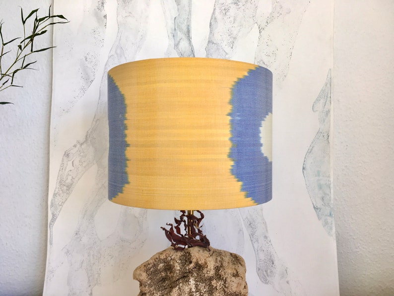 May include: A yellow and blue patterned lampshade with a natural stone base. The lampshade is made of fabric and has a unique ikat design. The base is made of a rough, textured stone.