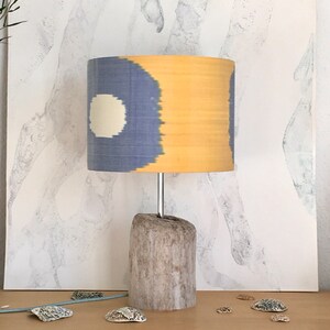 May include: A table lamp with a driftwood base and a blue and yellow patterned lampshade. The lampshade has a white circle in the center.