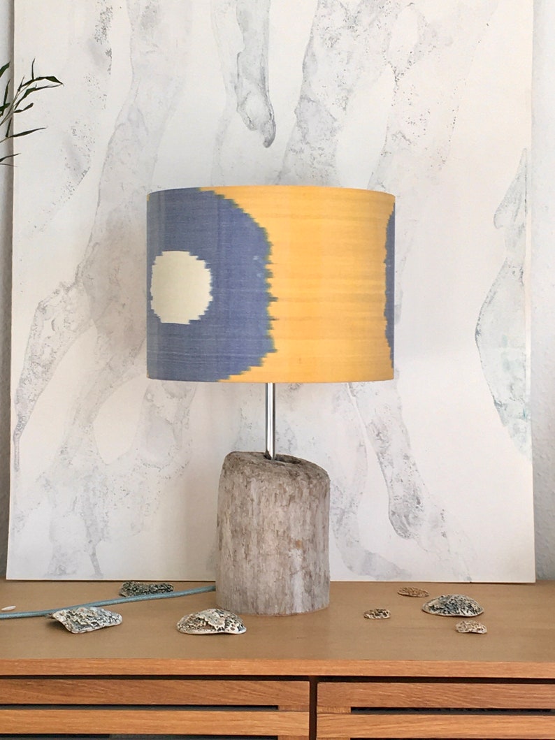 May include: A table lamp with a driftwood base and a blue and yellow patterned lampshade. The lampshade has a white circle in the center.