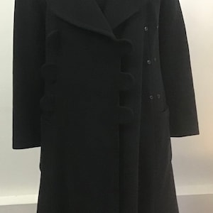 Pu&ograve; includere: Un cappotto di lana nero con un design unico che presenta un davanti con balze e una chiusura con un solo bottone. Il cappotto ha una silhouette lunga e aderente e un orlo leggermente svasato.