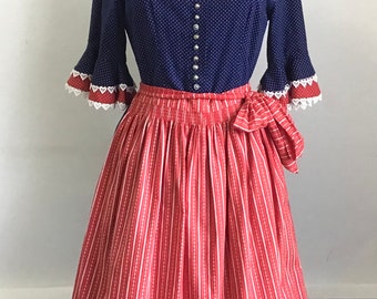 May include: A traditional-style dress with a navy blue polka-dot bodice and a red and white striped skirt. The dress features a square neckline, decorative trim, and a matching red necklace. The skirt has a bow at the waist.