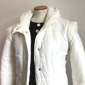May include: A white puffer jacket with a hood and a zipper closure. The jacket has a quilted design and is made of a lightweight material.