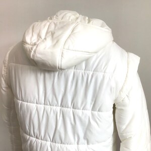 May include: White puffer jacket with a hood. The jacket has a quilted design and is made of a lightweight fabric.